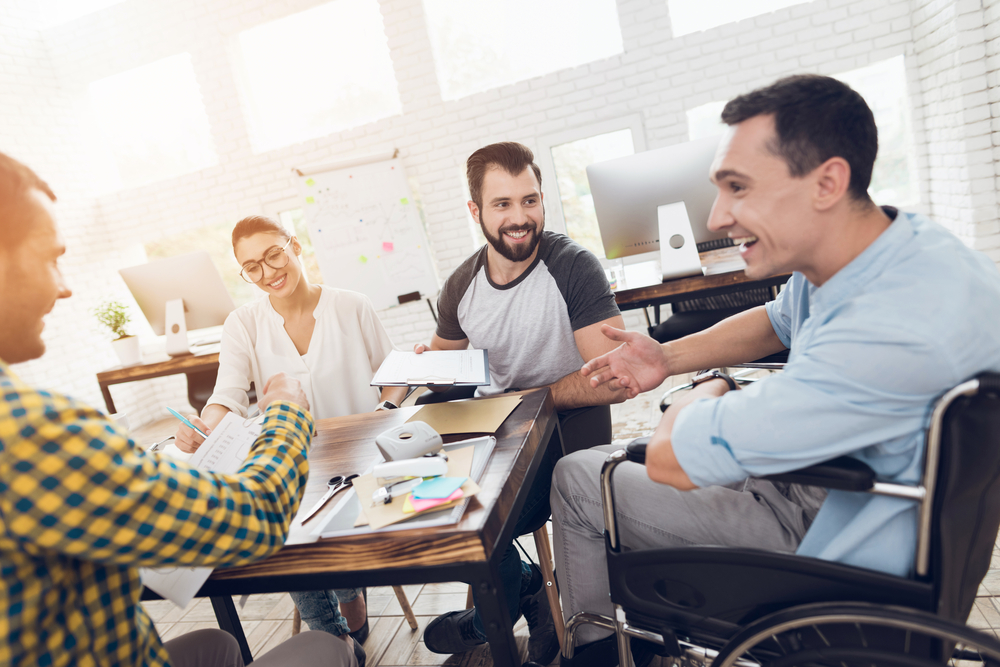 Employee in wheelchair conversing and laughing with fellow employees in business meeting