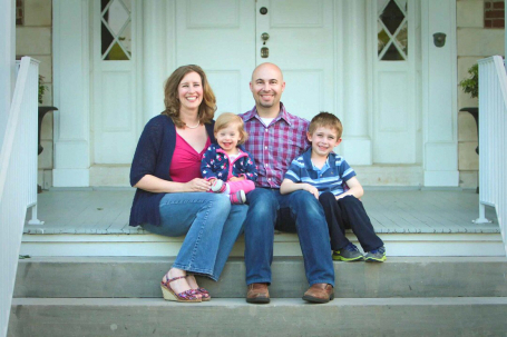 Valerie's husband and two children pose on the front steps of their house.