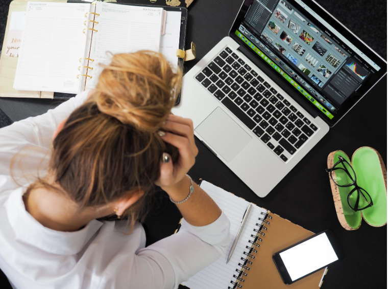 A woman sits with her head in her hands while looking down at her computer