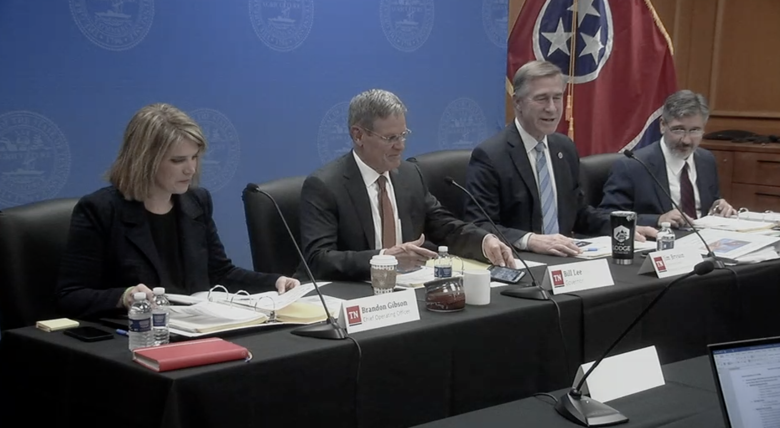 Governor Lee and his team Governor Lee and his cabinet sitting at a long table with papers in front of them and a Tennessee flag in the back