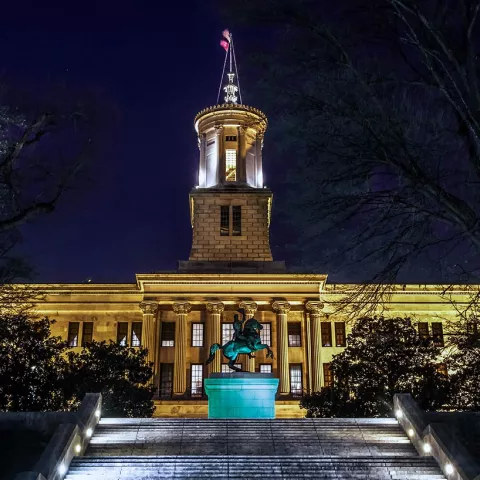 The Tennessee State Capitol building lit up at night and behind a set of ascending stairs