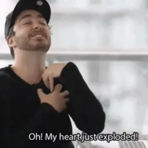 A man in a black long sleeve shirt and black hat curls his arms and says "oh! my heart just exploded!"