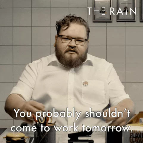 A man in a white button down shirt with brown curly hair is wearing glasses and saying "you probably shouldn't come to work tomorrow."