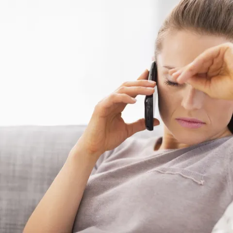 White woman sitting on a couch and talking on the phone and looking frustrated