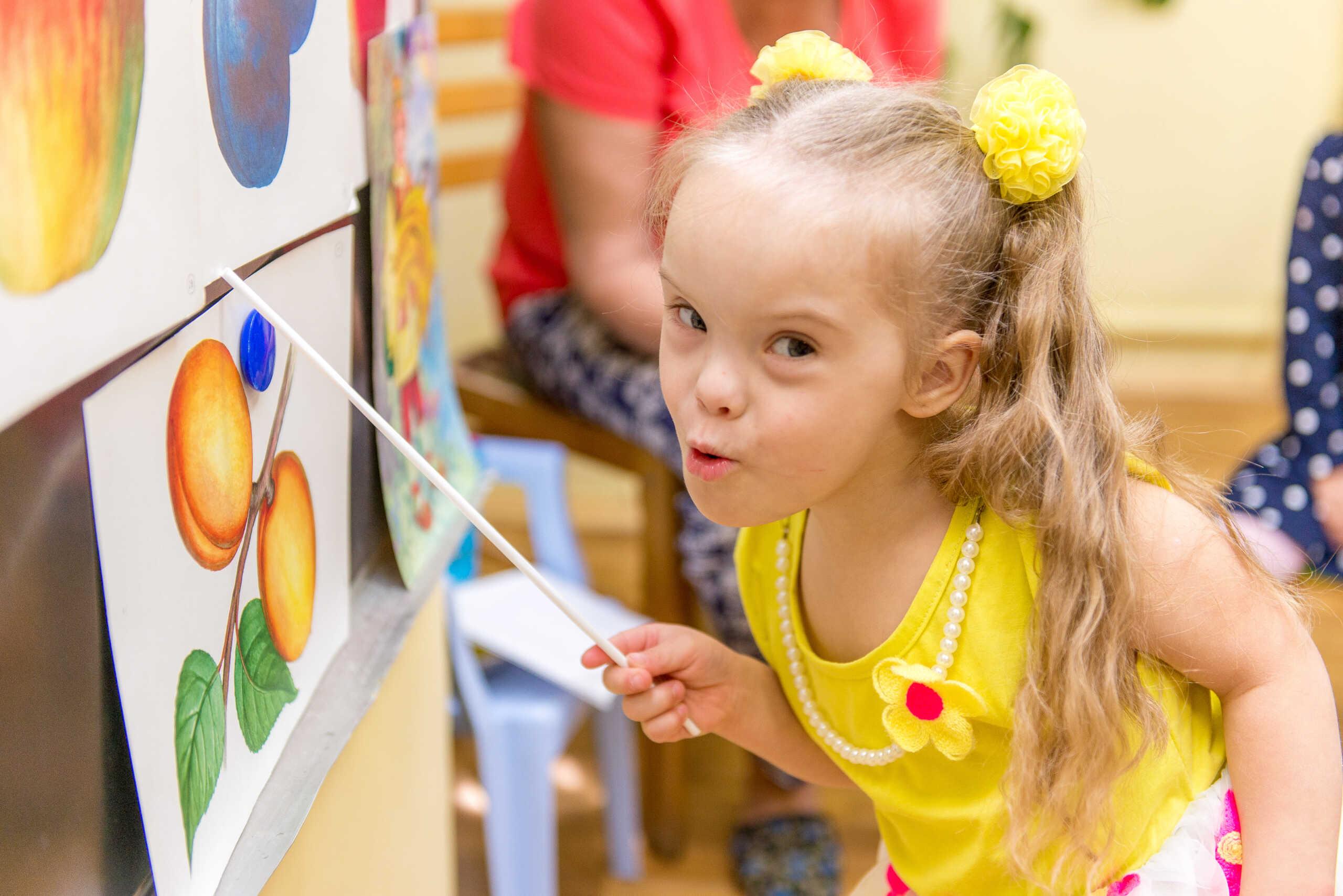 Young girl with Down syndrome wears pig tails and a smile at an easel