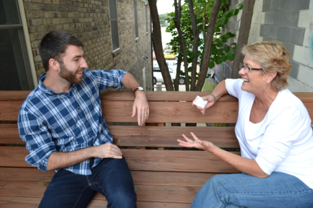 A man and a woman, co-workers, sit outside enjoying conversation with one another. 