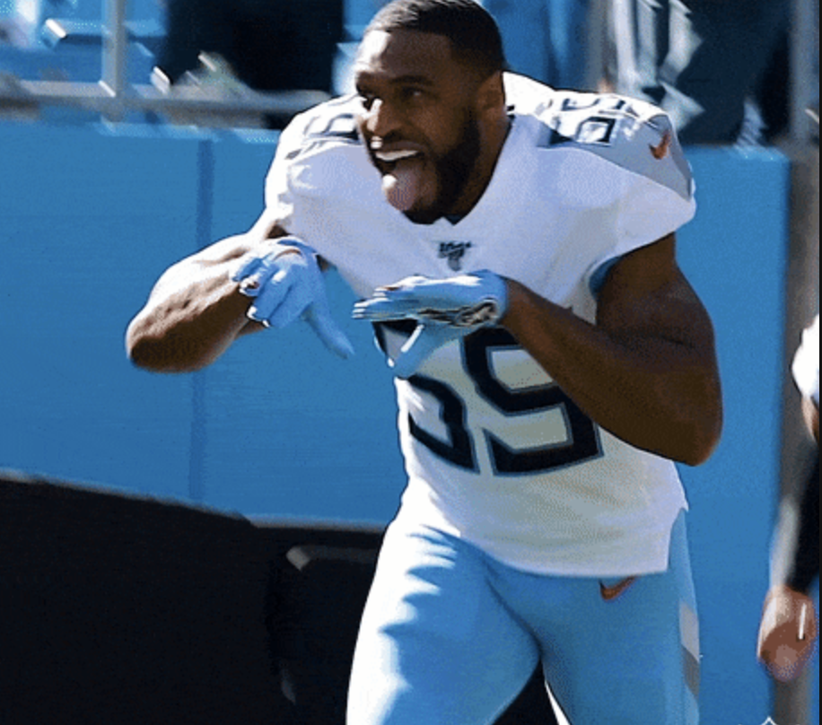 Titans football player in white jersey top and light blue jersey pants running onto the field with his tongue out